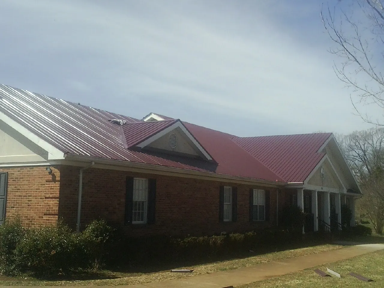 Red metal roof with gabled entries on a long brick building, from a Hail Damage Roof Repair job in Greensboro