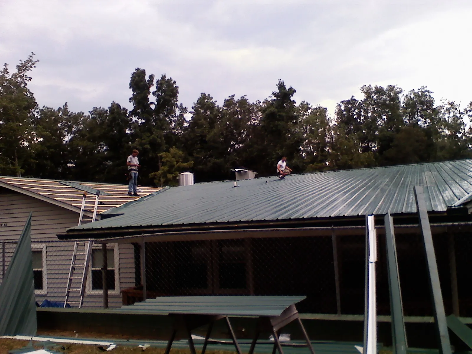 Two roofers installing green metal panels above a covered porch in Greensboro
